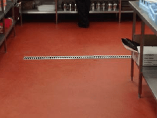 Hygienic epoxy floor installation with integrated stainless steel drainage grates for a food-grade facility.