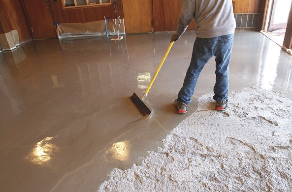 Applying high-flow self-levelling compound over a rough concrete floor to create a flat, uniform surface.