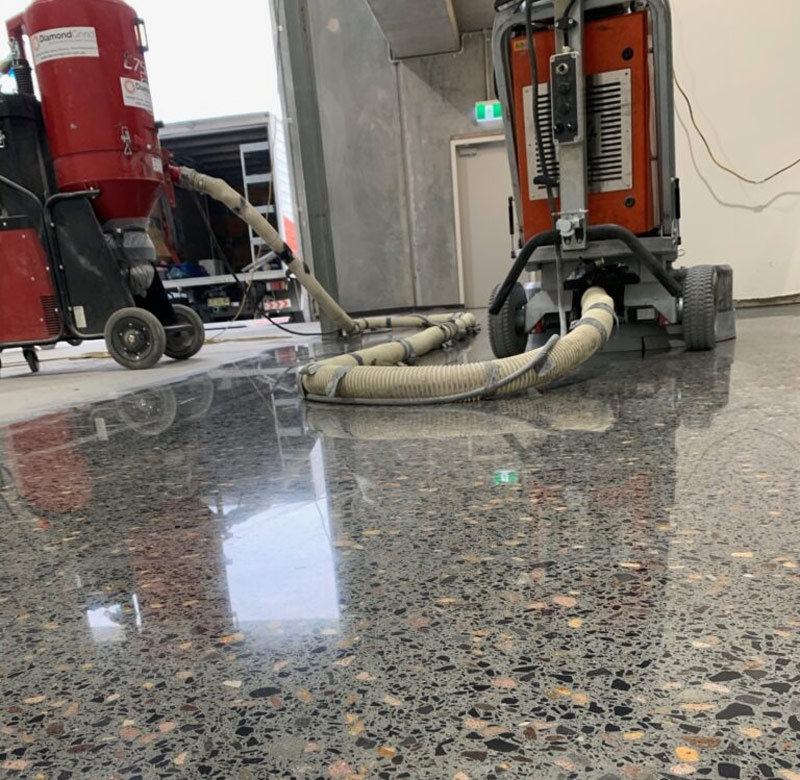 A polished concrete floor being prepared by a specialist using commercial diamond grinding machinery.